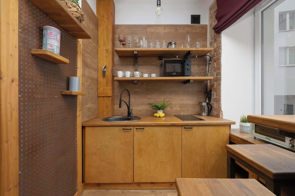 A compact wooden kitchenette with open shelves displaying glassware and cups, a small sink, and a microwave set into the cabinetry. The design emphasizes natural wood textures.