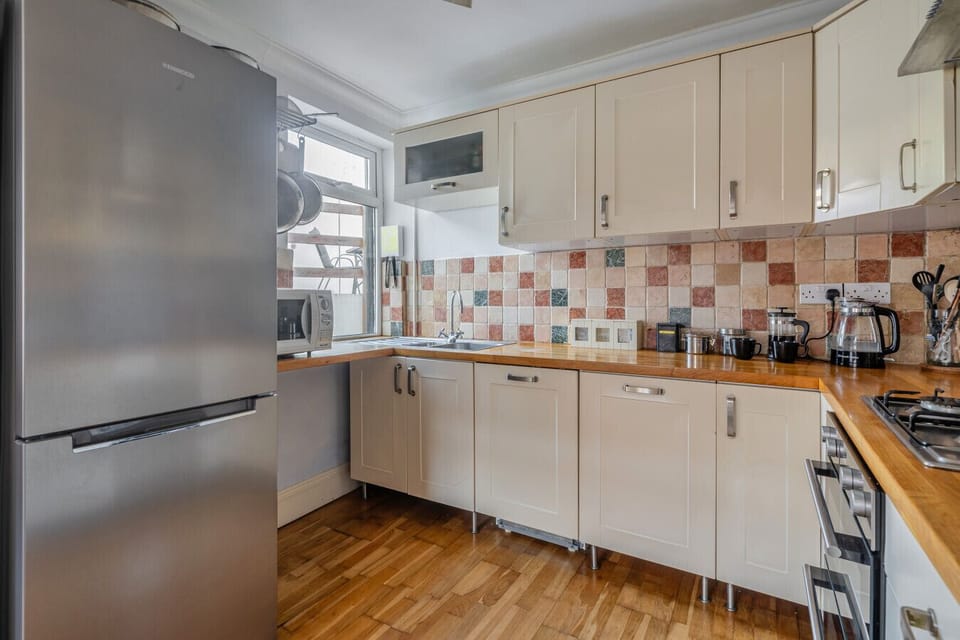 Kitchen with a large fridge-freezer, fitted white units, patterned tiled splashback and wooden worktop.