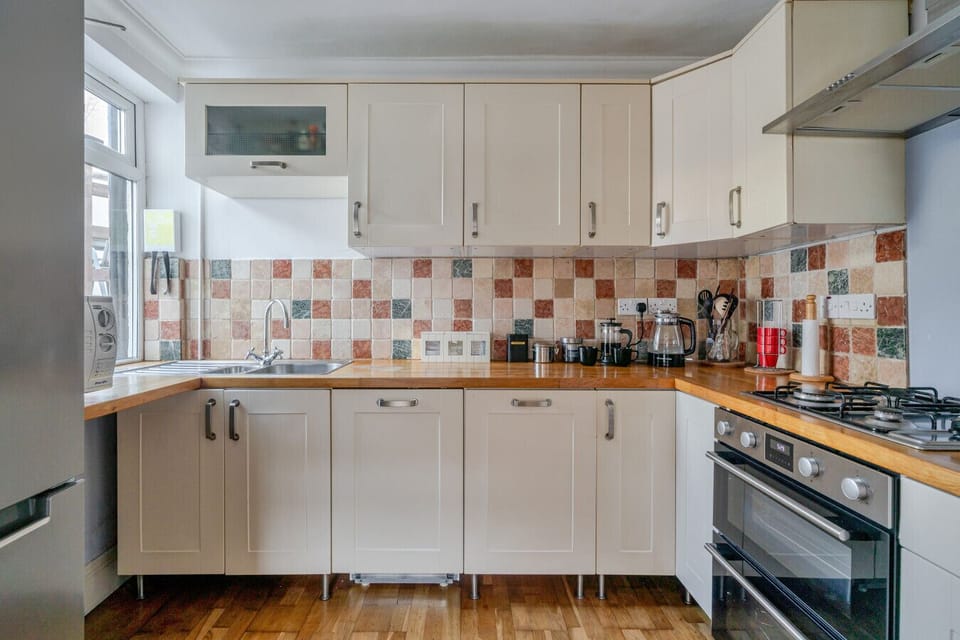 Fitted kitchen with white units, a patterned tiled splashback, wooden worktop, oven, gas hob and microwave.