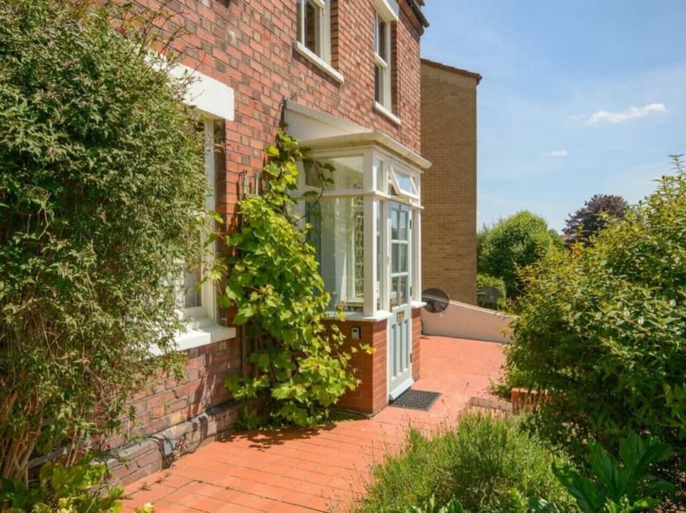 Side of the property showing a glazed porch entrance surrounded by mature climbing plants and garden greenery.