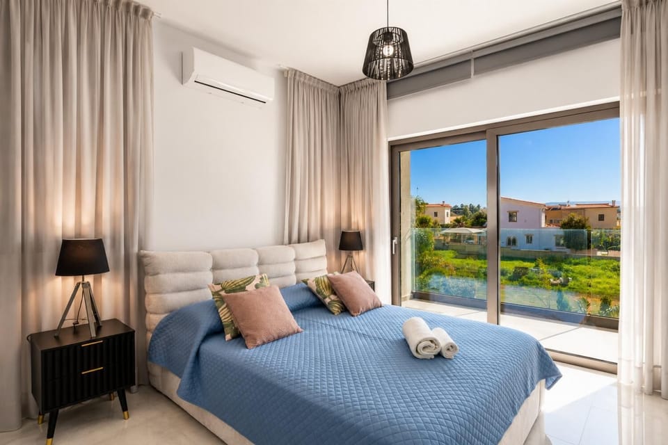 Bright modern bedroom with a blue bedspread, elegant grey curtains, and sunny balcony access.