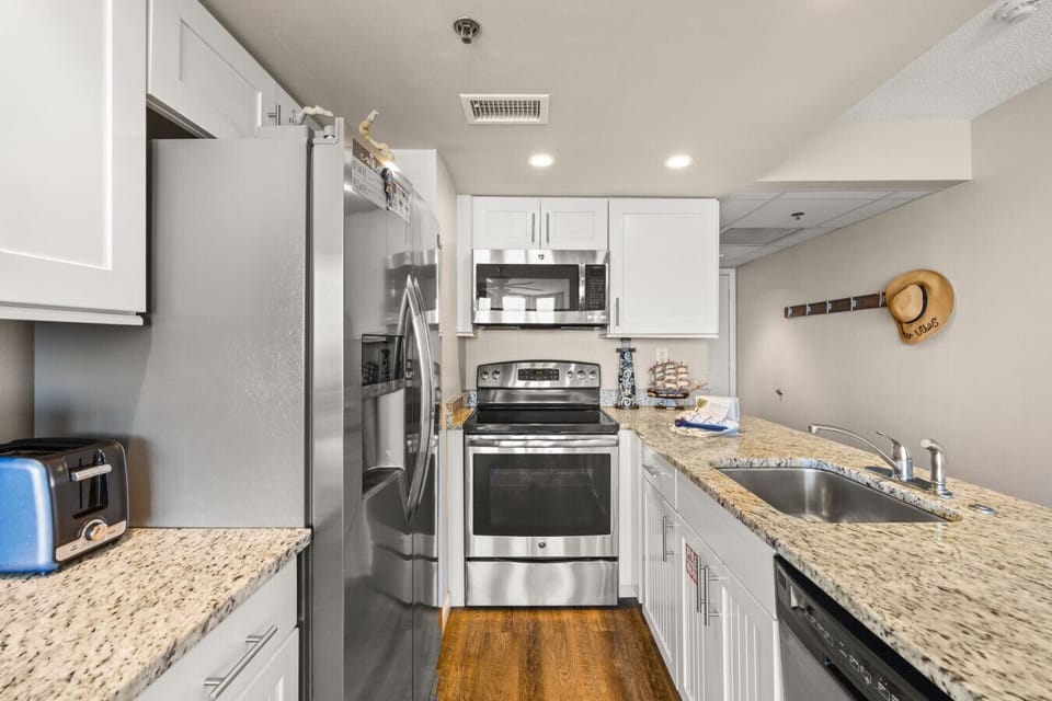 Modern coastal kitchen with granite countertops and stainless steel appliances, fully equipped for cooking during your beach stay