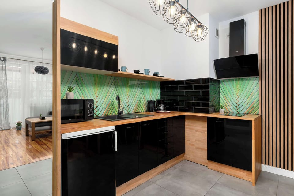 A sleek, modern kitchen is equipped with black cabinetry and a striking green glass backsplash. Built-in appliances, including a microwave and oven, are neatly integrated into the functional design.