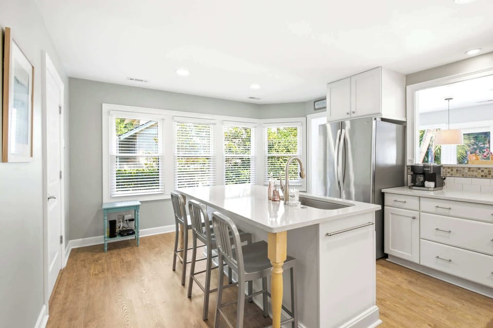 Polished quartz counters and stainless steel accents gleam in the soft morning glow of this airy kitchen. Wide windows invite the outdoors in, creating a bright and cheerful spot to gather for coffee at the central island.