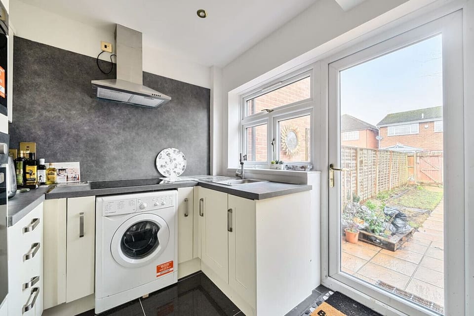 Kitchen with cream fitted units, an integrated washing machine, and a window that looks out directly to the rear patio and garden.