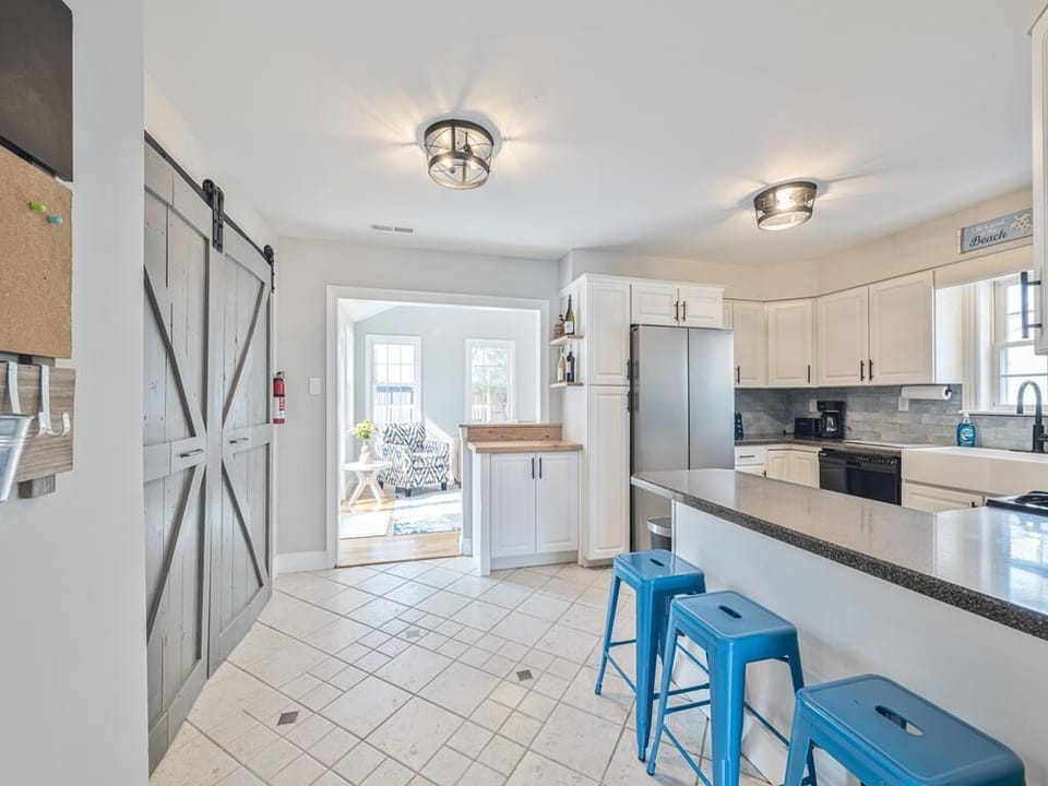 The spacious kitchen features modern coastal decor, complete with white cabinetry and vibrant blue stools.