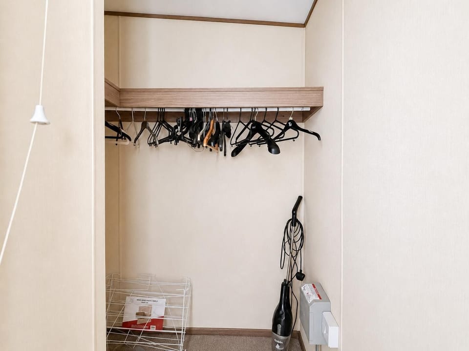 Closet space features a wooden hanging rail with multiple hangers and a vacuum cleaner stored below.