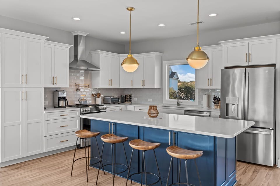 Bright coastal kitchen with white cabinets, stainless appliances, subway tile backsplash, and large blue island with bar seating in this Oak Island, NC beach home