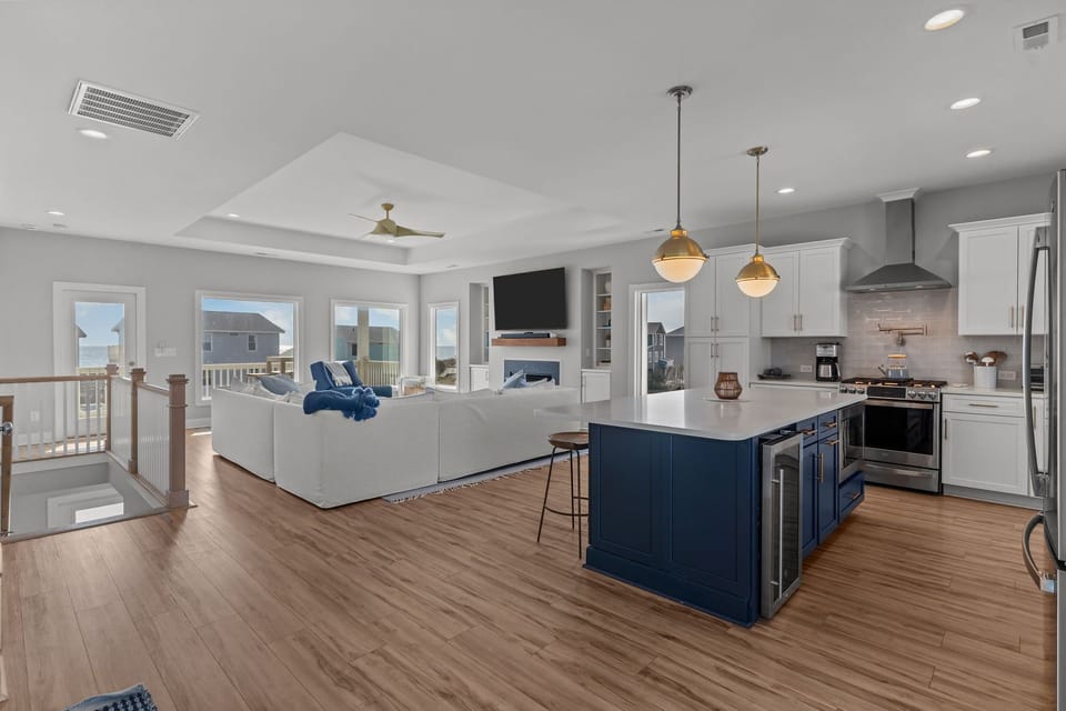Bright coastal kitchen with white cabinets, stainless appliances, subway tile backsplash, and large blue island with bar seating in this Oak Island, NC beach home