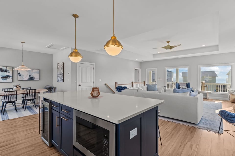 Bright coastal kitchen with white cabinets, stainless appliances, subway tile backsplash, and large blue island with bar seating in this Oak Island, NC beach home