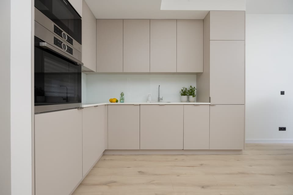 A sleek and modern kitchen with white cabinets and built-in appliances. The minimal design enhances the open-plan layout.