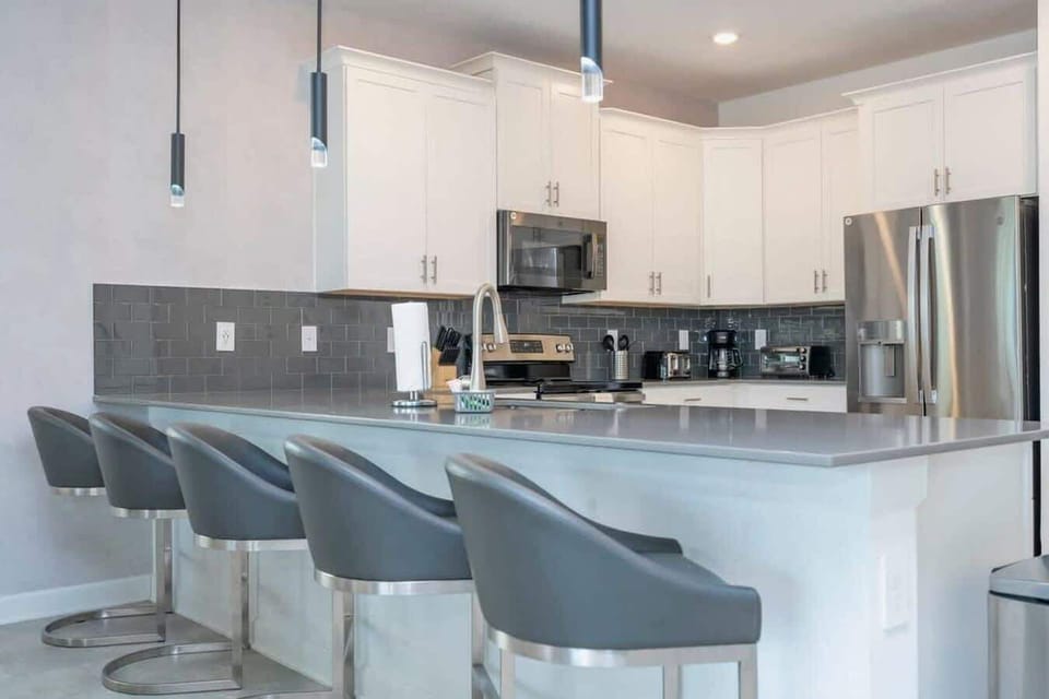 Modern kitchen with white cabinetry, stainless steel appliances, and sleek gray backsplash, perfect for preparing family meals and entertaining.