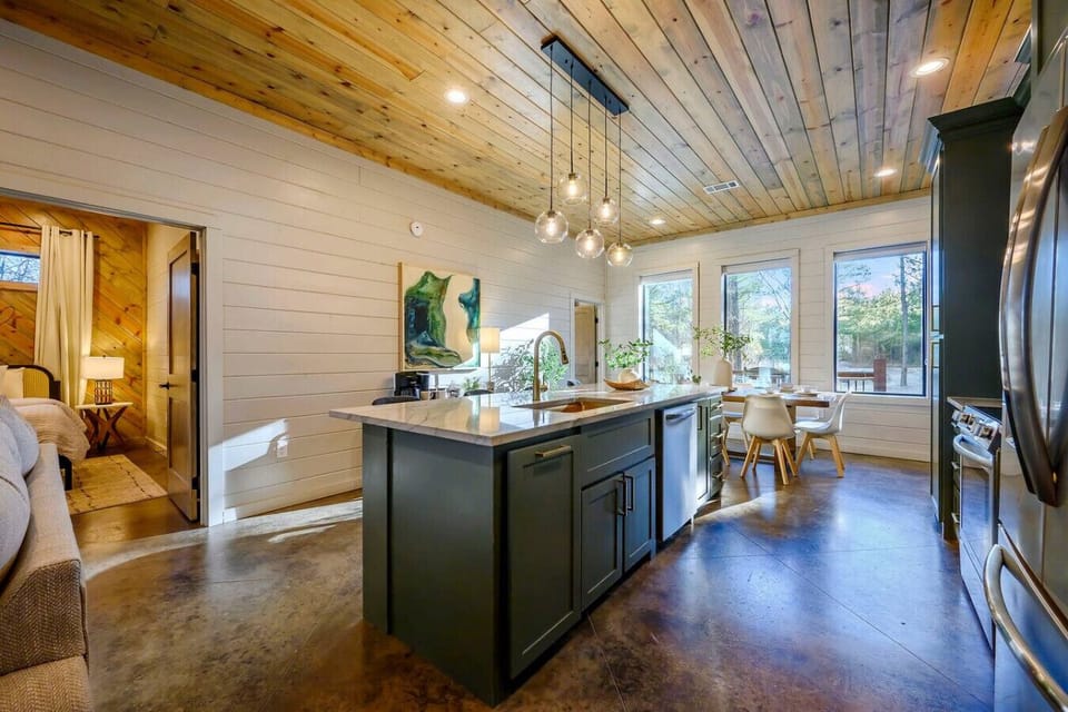 This stunning open-concept kitchen and dining area features soaring wood ceilings, a massive island, and walls of windows overlooking the trees.