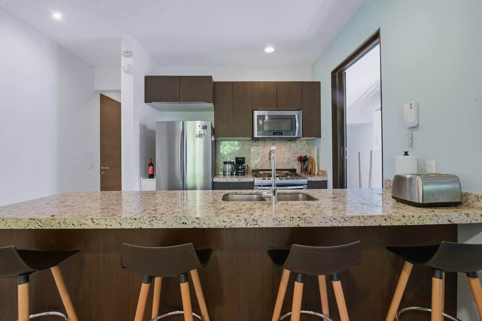 Fully equipped kitchen with a 4-burner stove, oven, microwave, coffee maker, blender, toaster, refrigerator with freezer, hot water kettle, and drinking water. The kitchen island with 4 stools is perfect for meals or gathering together.