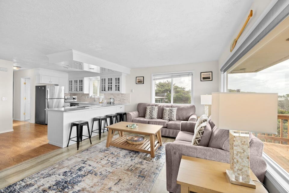 Relax in your open-plan living space with modern kitchen, cozy seating, and beautiful views through large windows.