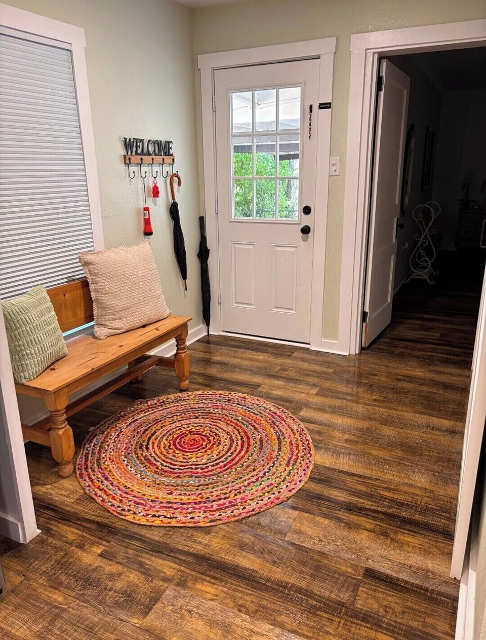 Welcoming side entryway with bench seating, hooks, and a colorful braided rug