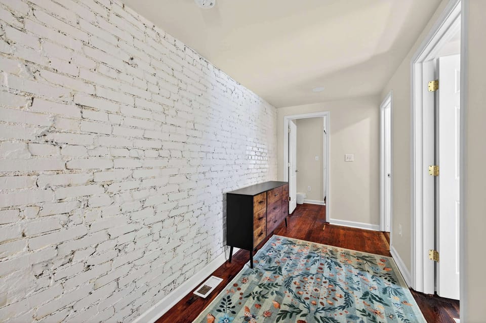 Light-filled corridor with exposed brick charm leading to serene, private sleeping spaces.