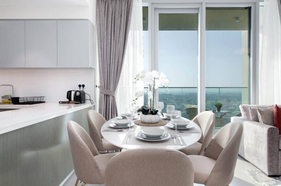 Elegant Dining Area with Balcony Views: Stylish round dining table set for four, positioned beside floor-to-ceiling windows with beautiful balcony and city views in this luxury 2BR Downtown Dubai apartment.