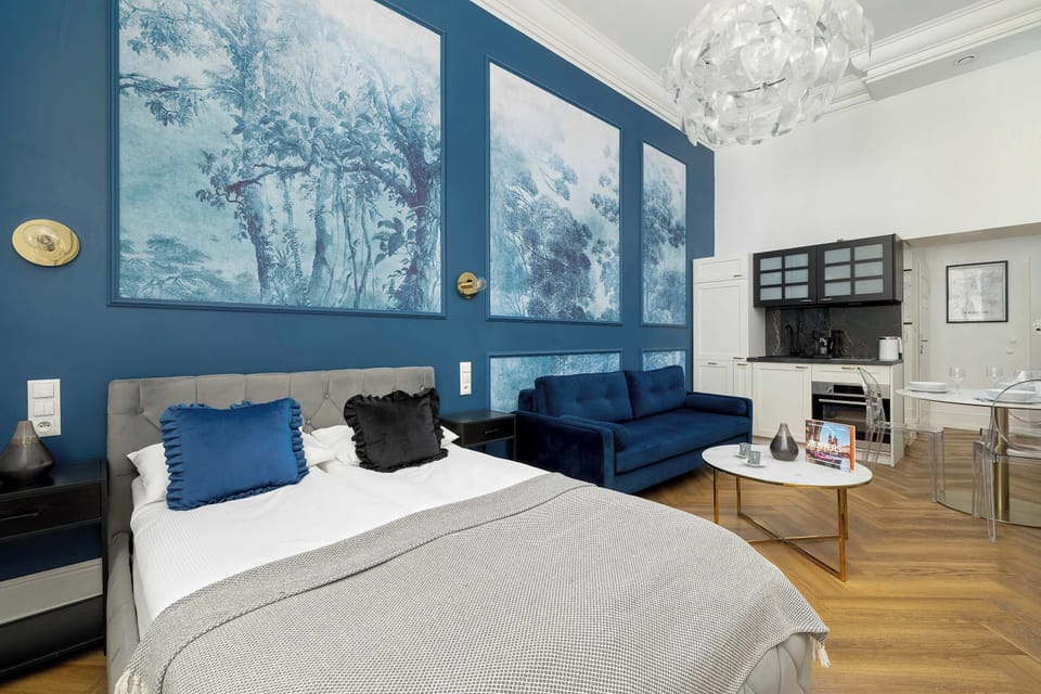 A interior view blending the bedroom and living room into one cohesive composition. The blue sofa, large artwork panels, and white furnishings create a harmonious contrast.
