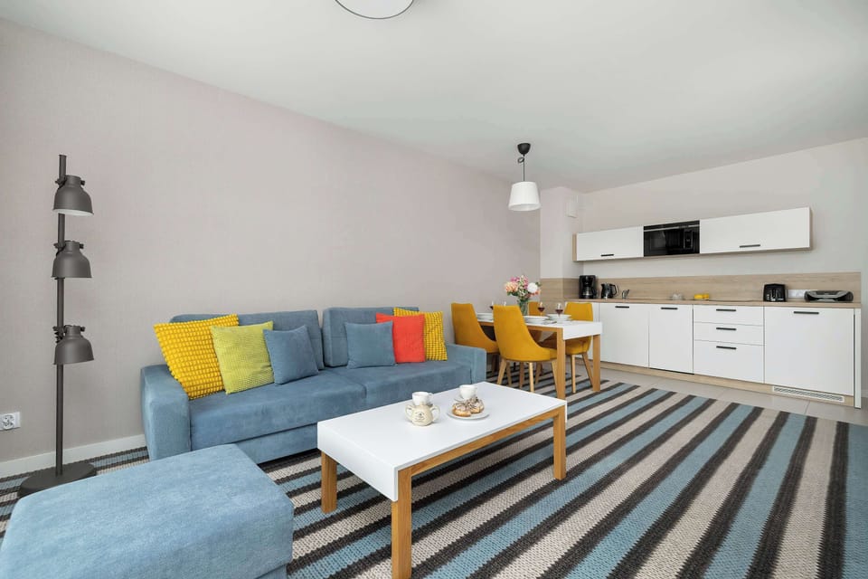 Modern white cabinetry lines the wall, complemented by a sleek black microwave and essential kitchen appliances. The dining table with sunny yellow chairs creates a cheerful spot for morning coffee.