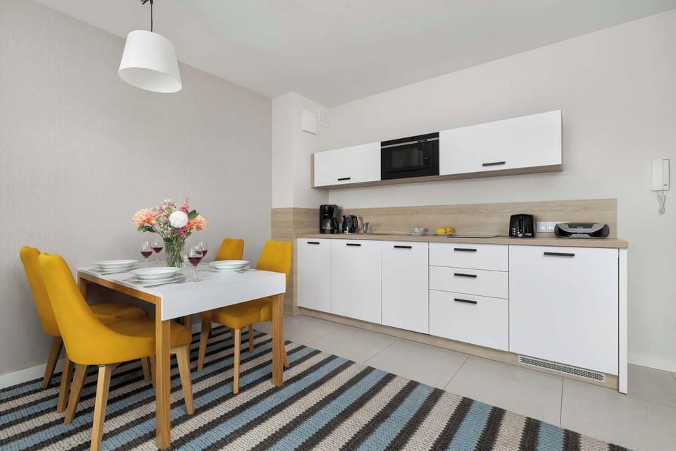 The white kitchenette furniture is paired with a light wood-textured backsplash, creating a clean and warm aesthetic. High-quality appliances, including an electric kettle and coffee maker, are ready for guest use.