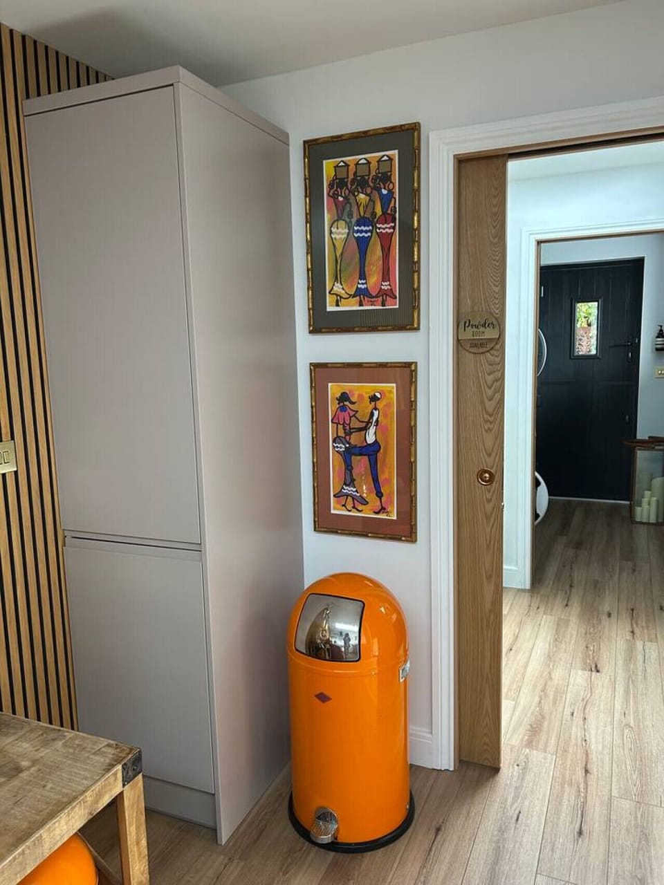 An internal hallway with a door leading to the shower room, two framed pictures on the wall, and an orange pedal bin on a timber floor.