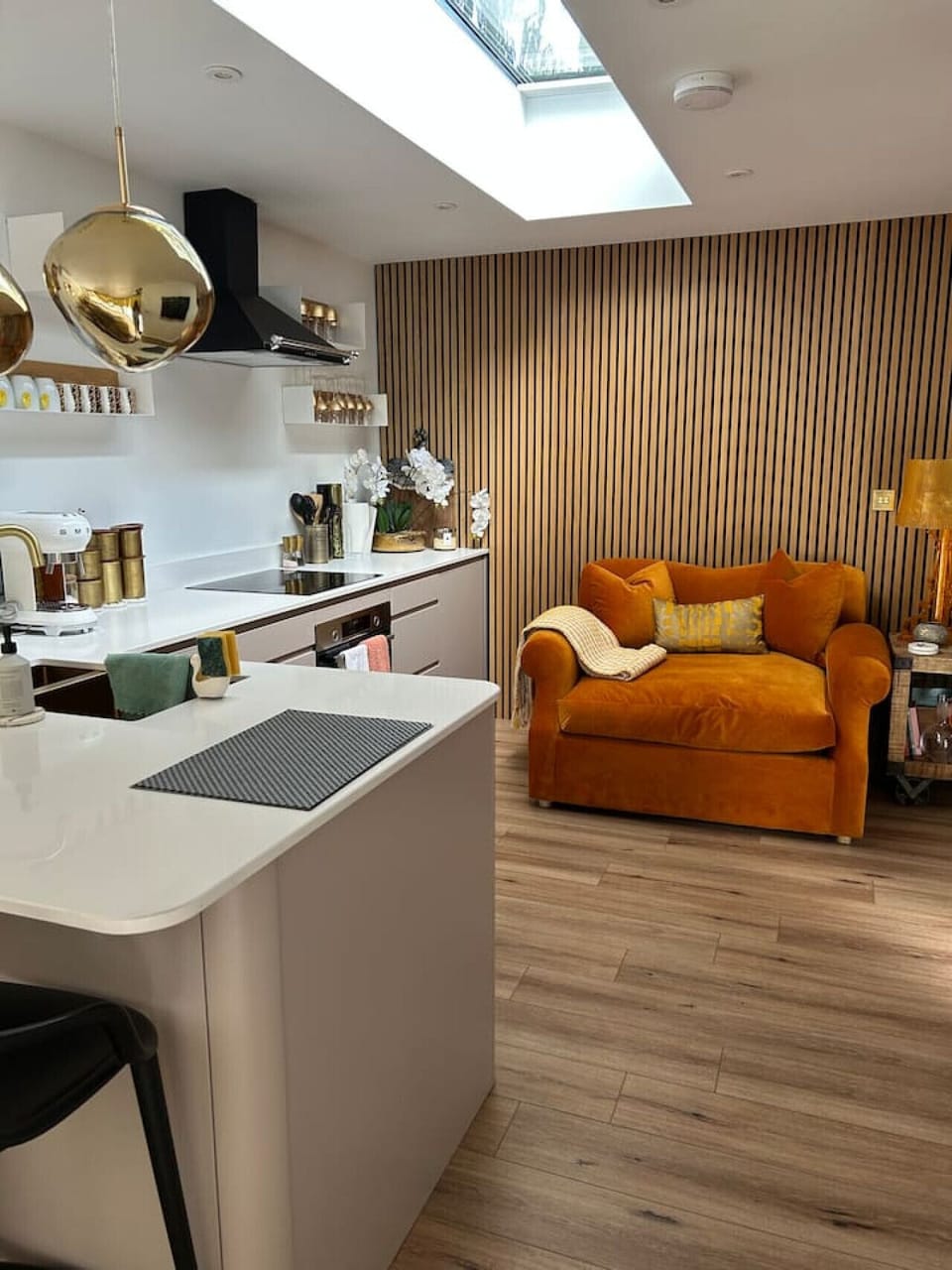 Kitchen area showing a white worktop, induction hob, a vertical wooden slat feature wall, and a skylight set into the ceiling above.