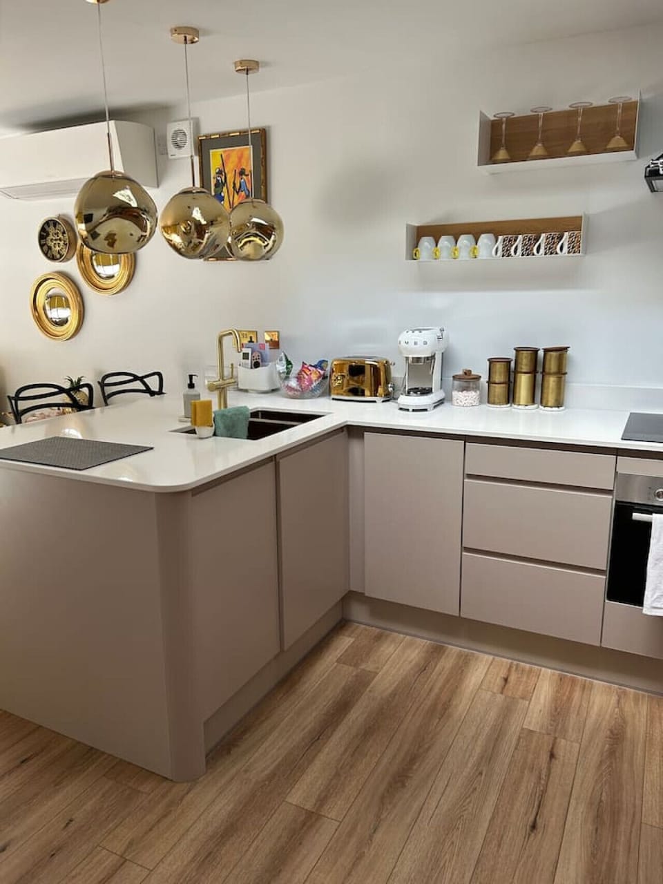 L-shaped kitchen with white worktops, a range of appliances including a dishwasher and oven, open shelving, and brass-finish pendant lights overhead.