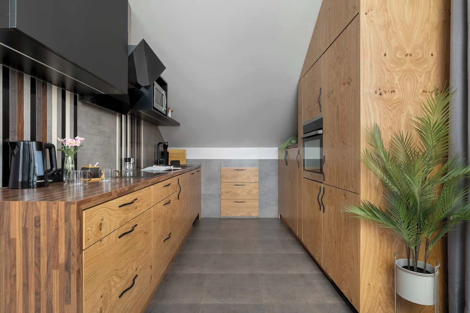 A modern kitchen with wooden cabinets, a black countertop, and built-in appliances. The room is well-lit and spacious for cooking.