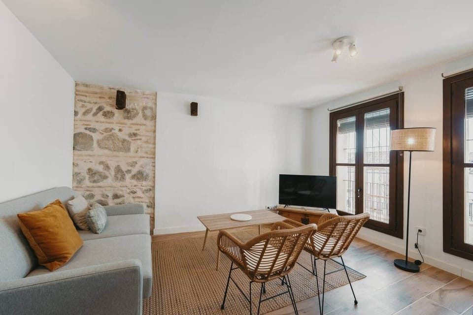Salón con sofá, sillas de mimbre y pared de piedra original