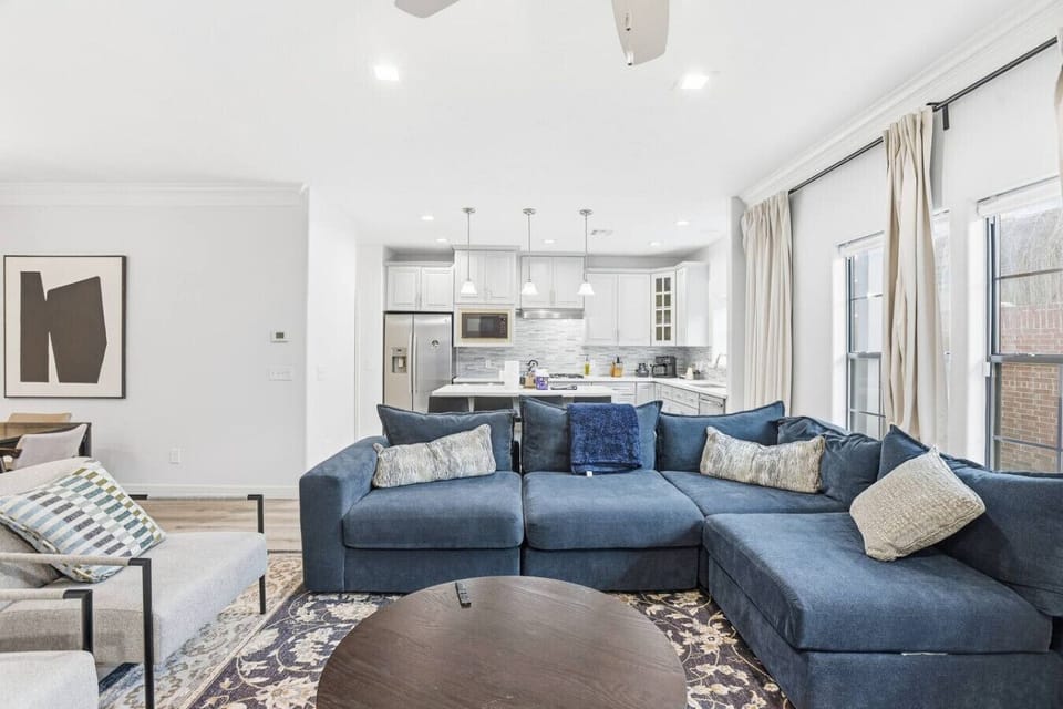 Spacious open-concept living area with a deep sectional sofa, stylish accents, and views into the bright kitchen—ideal for movie nights, lounging, or entertaining together