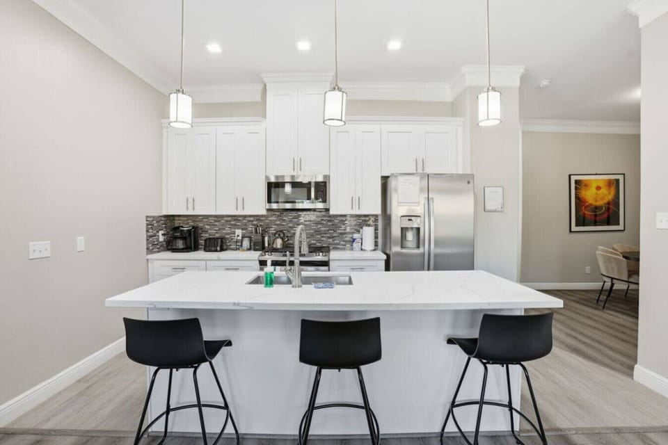 Spacious modern kitchen with oversized island seating, sleek white cabinetry, and stainless appliances. Perfect for shared meals or morning coffee—gather around the island, prep with ease, and enjoy an open layout designed for group stays.