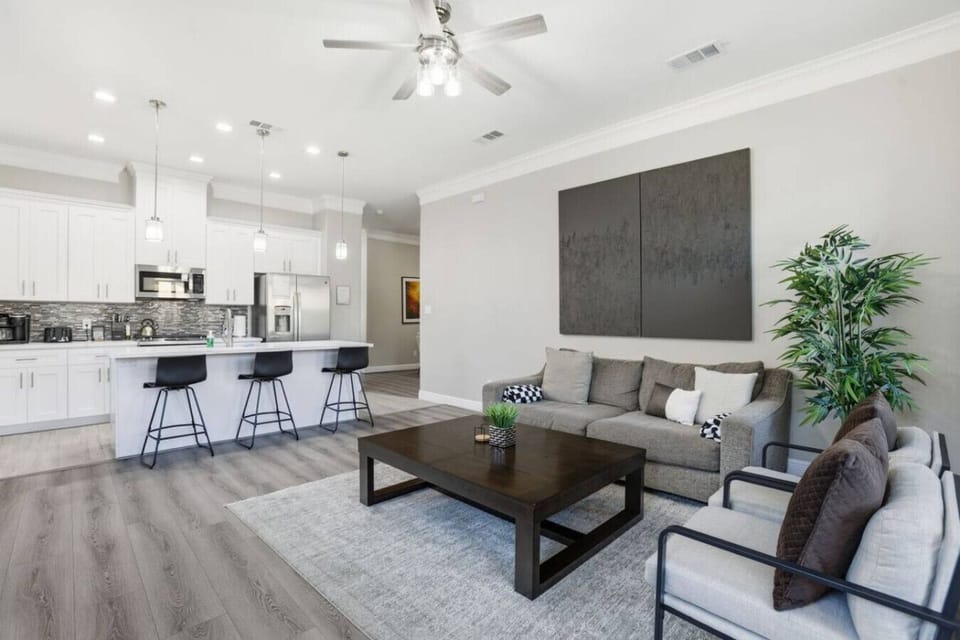 Open-concept living meets a bright modern kitchen with island seating. Relax on comfy sofas, enjoy movie nights, or gather around the coffee table—perfect for groups, families, and easy entertaining in a stylish, airy space.