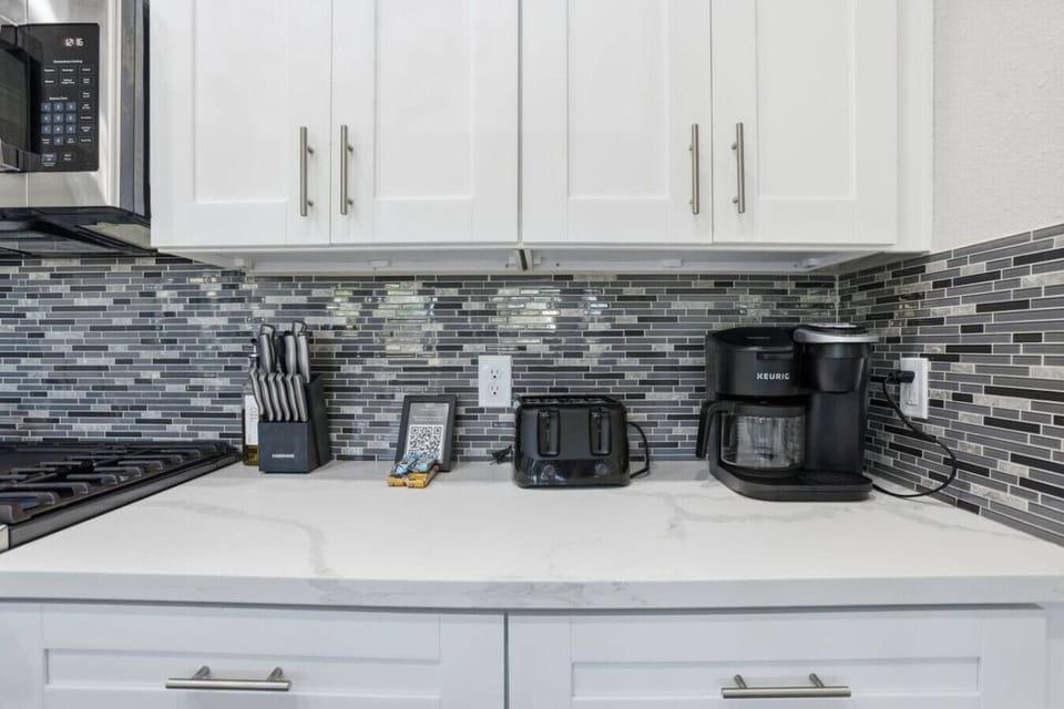 Clean, modern kitchen counter with white cabinetry, sleek backsplash, and coffee station—fully equipped for easy meals, morning coffee, or quick snacks during your stay.