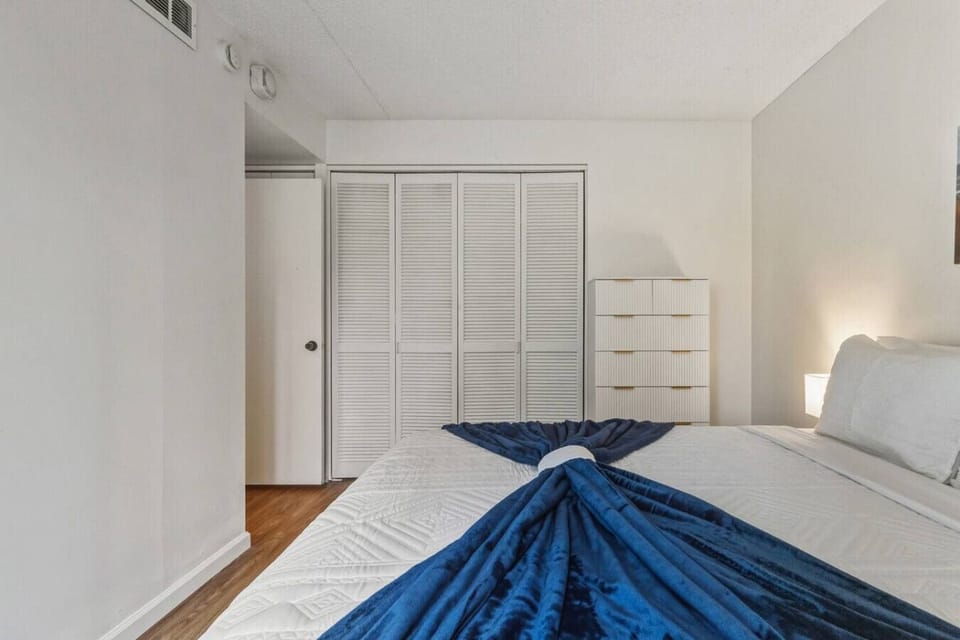 Rest easy in modern calm.   White walls, wood floors, and a fan-folded blanket set the tone for quiet nights.