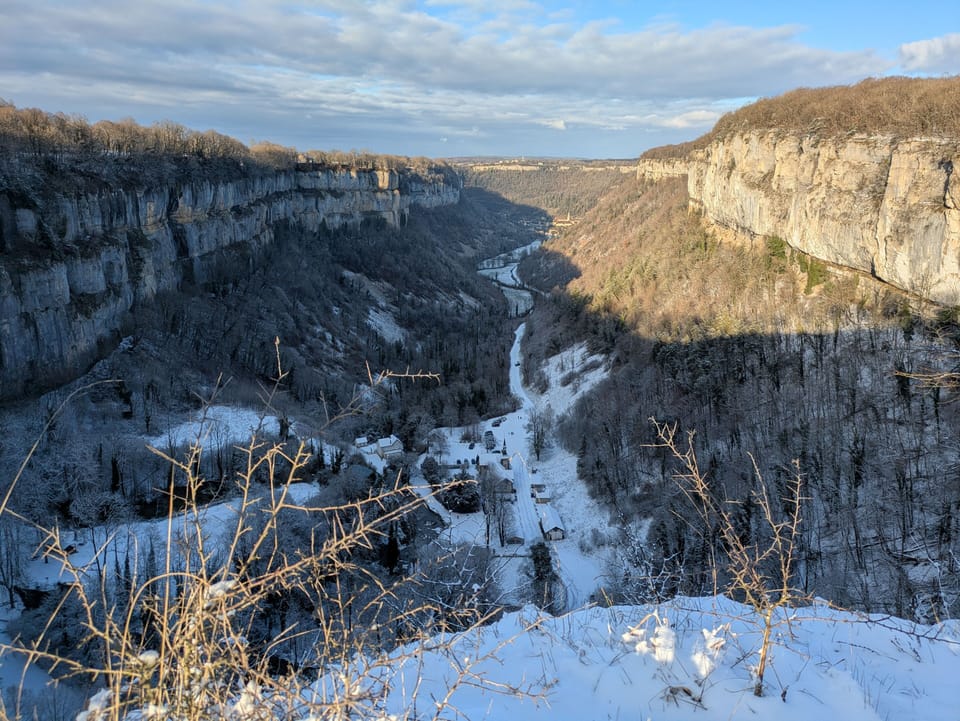 Snow blankets a rugged canyon in winter, revealing the striking natural beauty of the Jura cliffs under a crisp blue sky.