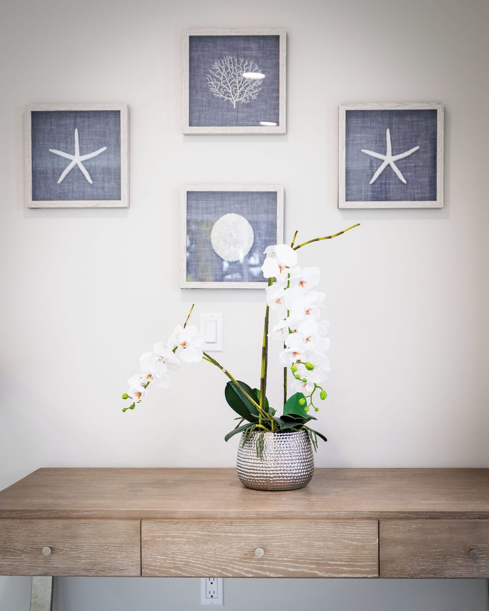 Nautical-themed framed art and white orchids on a wood console.
