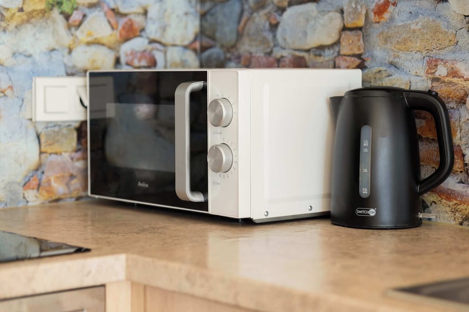 Kitchen countertop with visible appliances in the form of a microwave oven and electric kettle, placed against a stone wall. These appliances provide convenience when preparing quick meals and drinks.