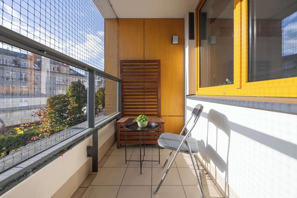 A balcony with a railing, from which you can admire the view of the neighborhood and the blue sky, is the perfect place to take a breath of fresh air. The balcony has a small table and chair, perfect for morning coffee.