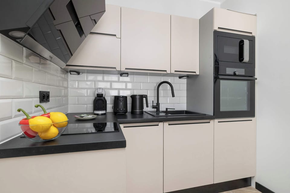 A functional kitchenette workspace with a black countertop, modern sink, and small appliances like a toaster and kettle.