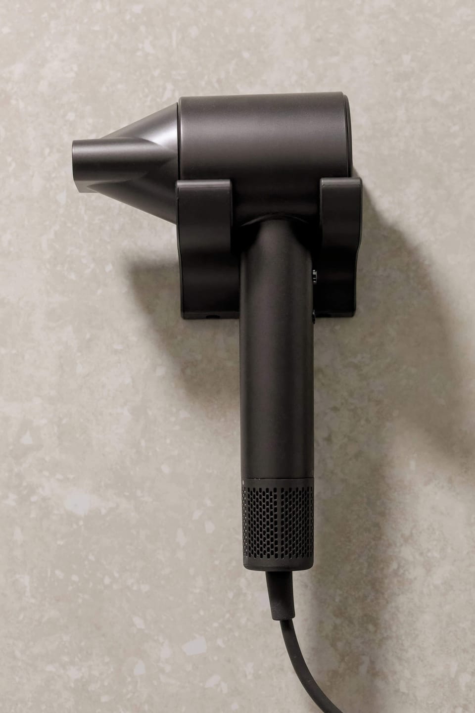 A close-up of a professional black hairdryer mounted on the bathroom wall for guest convenience.