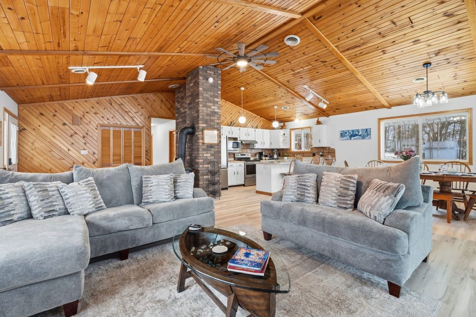 Spacious open-concept living room with vaulted wood ceilings, comfortable seating, and a fully equipped kitchen and dining area perfect for gathering.