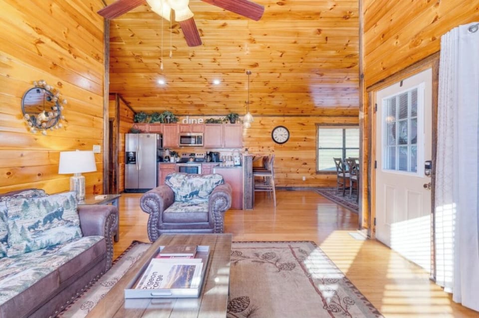 Relax in your cozy cabin's open living space, where warm wood walls and rustic furnishings create the perfect mountain retreat atmosphere.