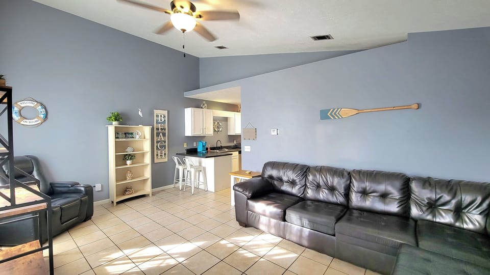 Spacious living area with a leather sofa, recliner, ceiling fan & kitchen bar