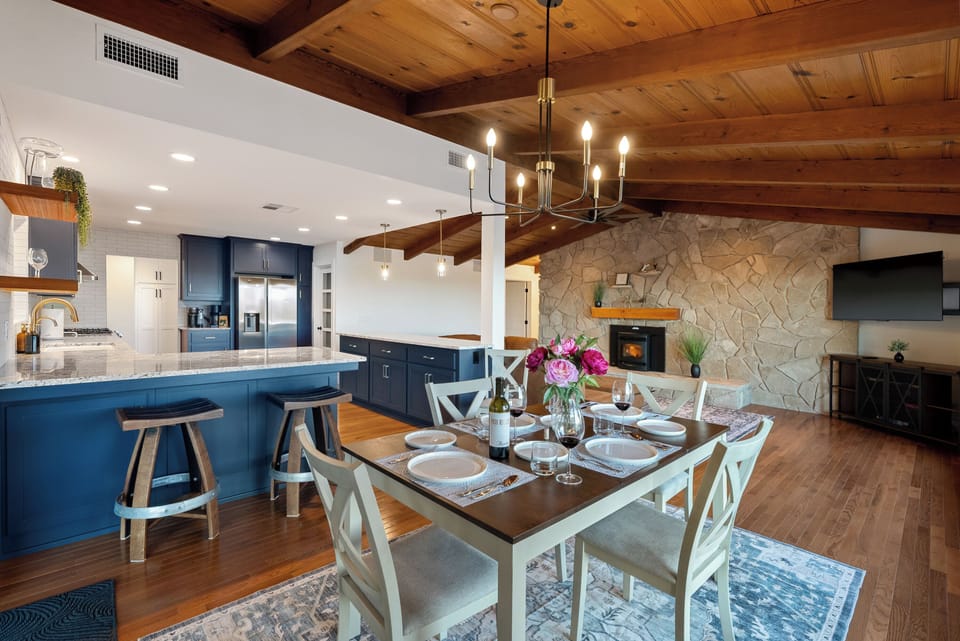 This expansive hillside retreat combines modern navy architecture with warm, rustic interiors featuring an open-concept kitchen, a floor-to-ceiling stone fireplace, and a tiered brick patio complete with a private hot tub and panoramic valley views.