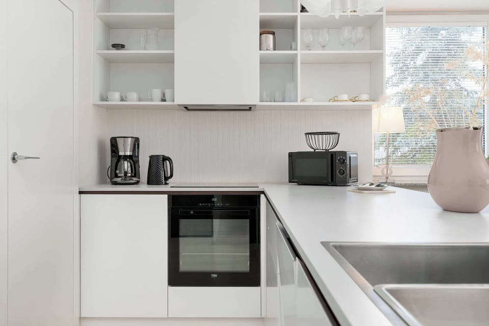 Modern white kitchenette with built-in oven, open shelving, and practical countertop workspace.