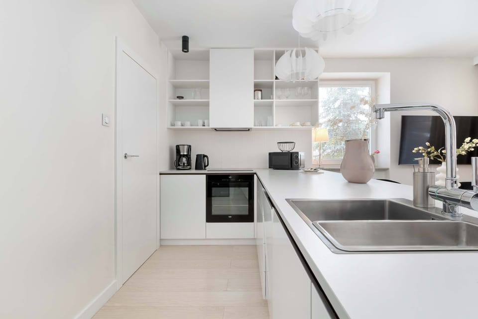 Modern white kitchenette with built-in oven, open shelving, and practical countertop workspace.