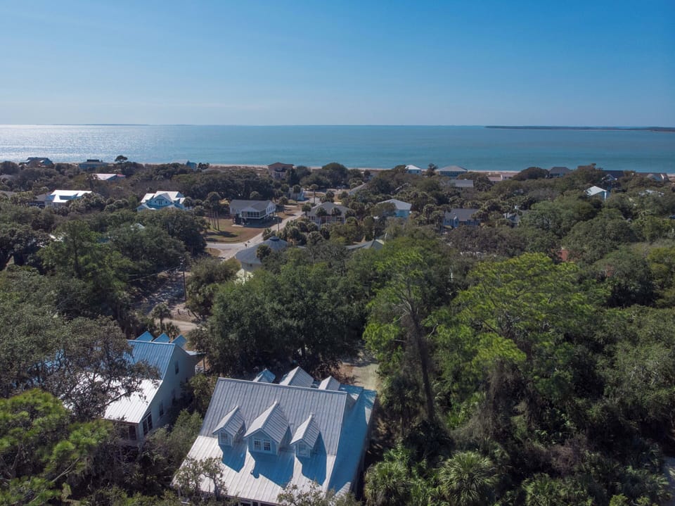 Aerial view of coastal property nestled among lush trees, just minutes from pristine beaches and charming neighborhood homes.