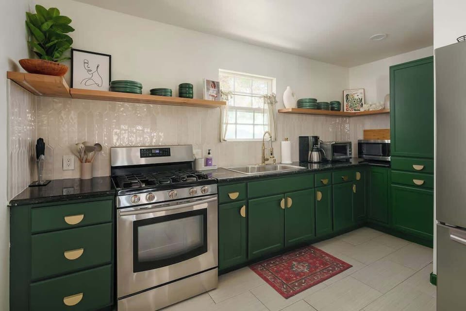 Bright kitchen with green cabinets, stainless appliances, and open shelving for easy meal prep