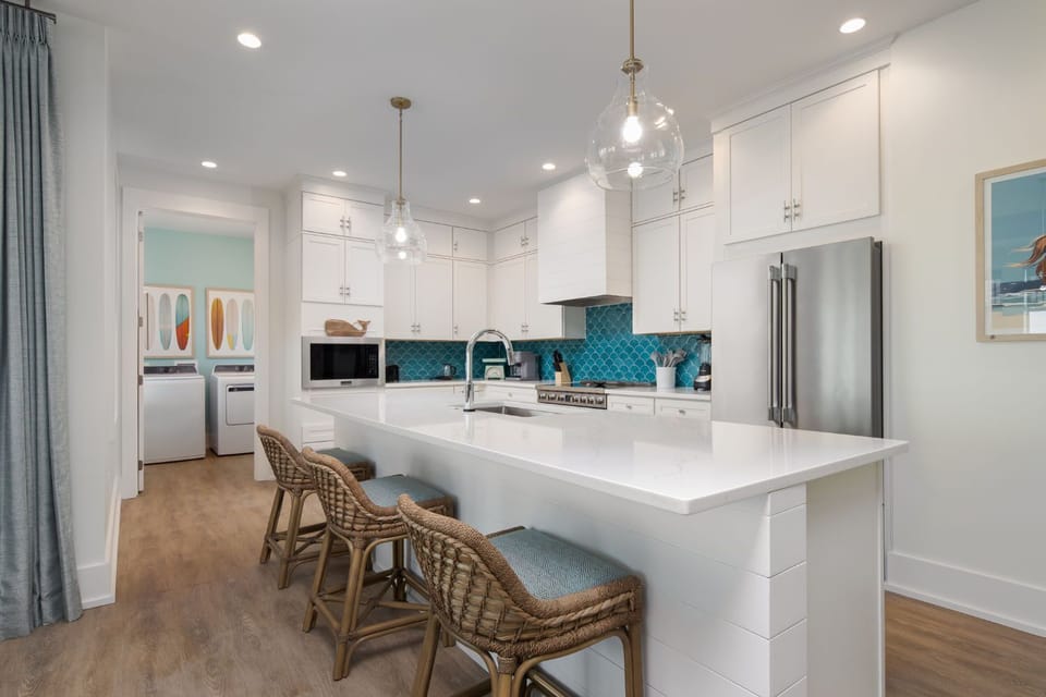 This modern kitchen features sleek white cabinetry and vibrant teal backsplash, complemented by stylish bar seating for casual gatherings.